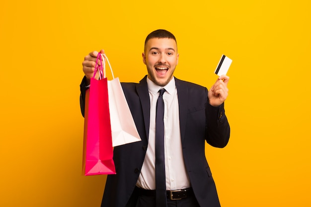 Young handsome businessman  against flat wall with shopping bags