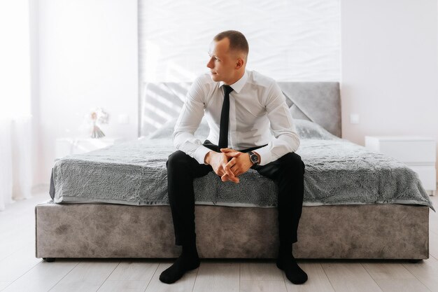 Young handsome businessman sitting on bed in hotel room The groom is preparing for the wedding