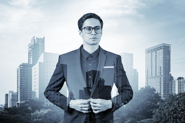 Young handsome businessman in suit and glasses dreaming about new career opportunities after MBA graduation Bangkok on background Double exposure