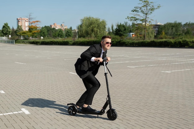 Young handsome businessman in a suit rides an electric scooter around the city and laughs