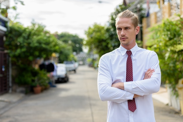 Young handsome businessman thinking with arms crossed outdoors