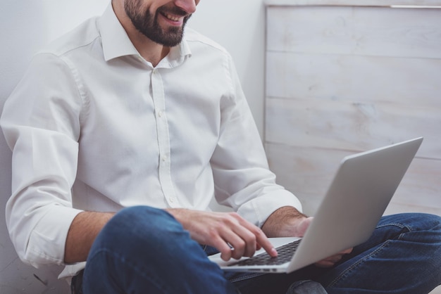 Young handsome businessman in white classical shirt and jeans using a laptop while working closeup