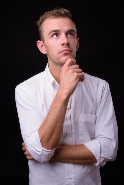  young handsome businessman with blond hair against black wall