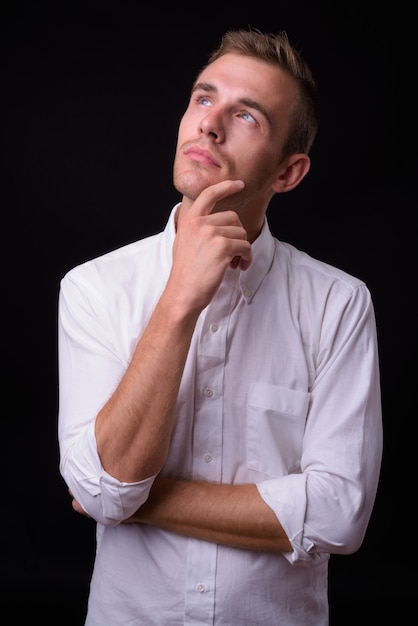  young handsome businessman with blond hair against black wall