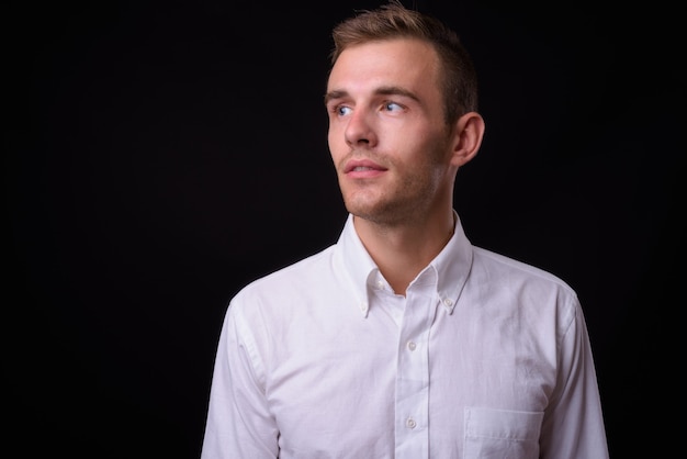  young handsome businessman with blond hair against black wall