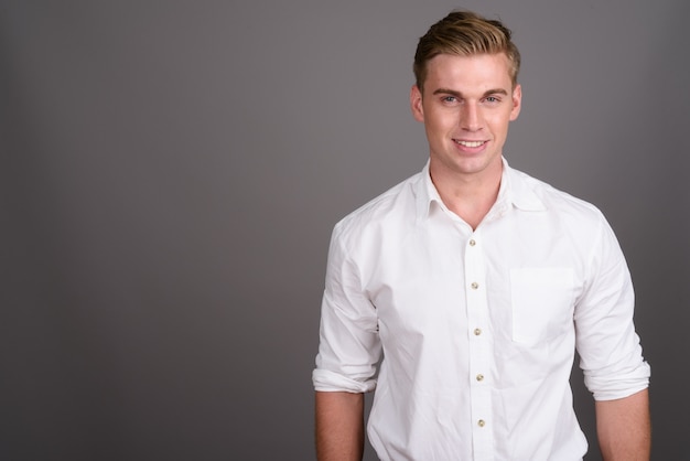 Young handsome businessman with blond hair on grey wall