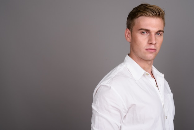 Young handsome businessman with blond hair on grey wall