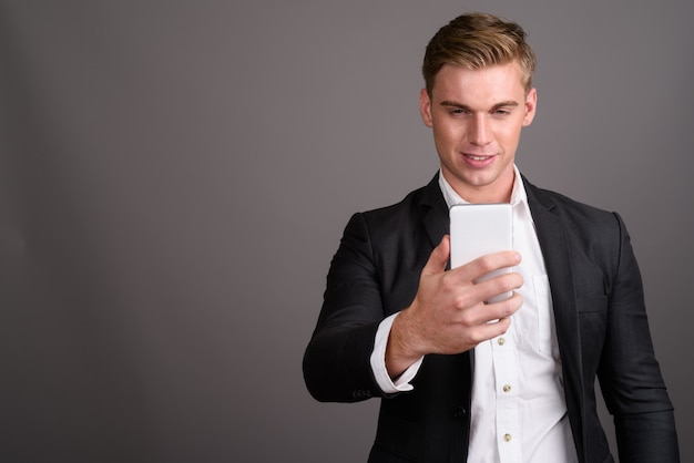 Young handsome businessman with blond hair wearing suit on grey wall