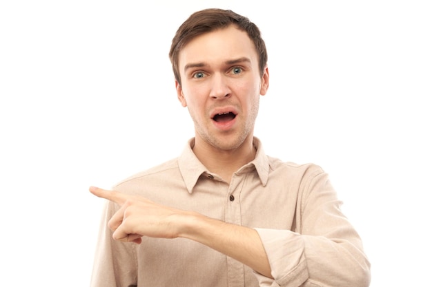 Young handsome caucasian brunette man in casual shirt points finger at empty space isolated on white background with copy space. Demonstrates product, excitedly shows something