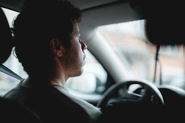 Photo young handsome caucasian guy looks behind the road while driving a car on a rainy day