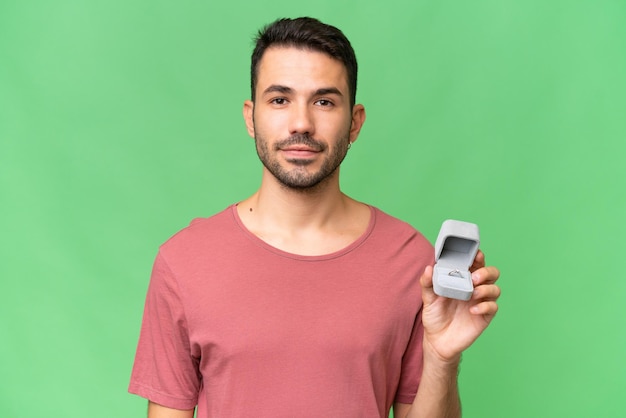 Young handsome caucasian man holding a engagement ring over isolated background smiling a lot