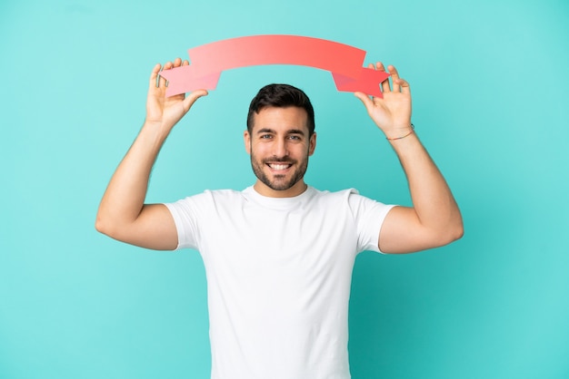 Young handsome caucasian man isolated on blue background holding an empty placard