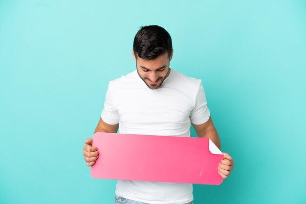 Photo young handsome caucasian man isolated on blue background holding an empty placard