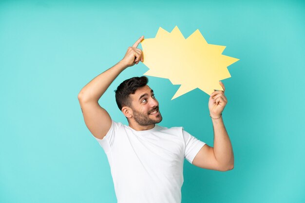 Young handsome caucasian man isolated on blue background holding an empty speech bubble and having doubts