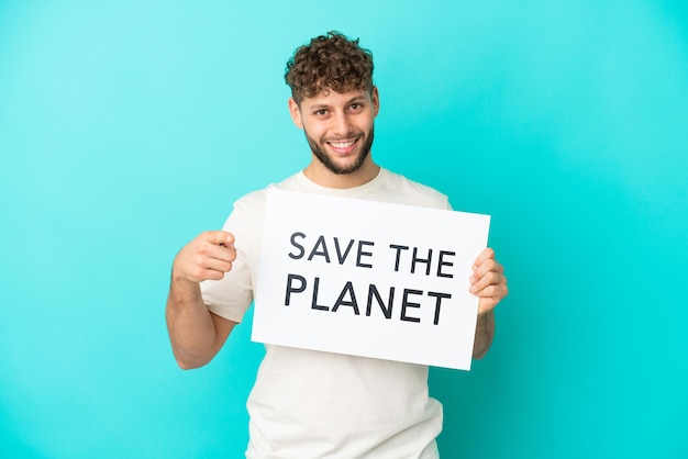 Young handsome caucasian man isolated on blue background holding a placard with text Save the Planet and pointing to the front