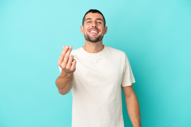 Young handsome caucasian man isolated on blue background making money gesture