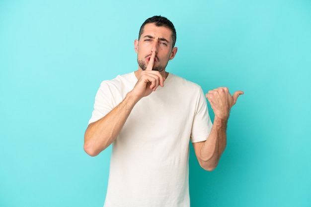 Young handsome caucasian man isolated on blue background pointing to the side and doing silence gesture