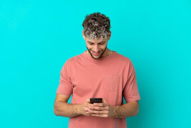 Photo young handsome caucasian man isolated on blue background sending a message with the mobile