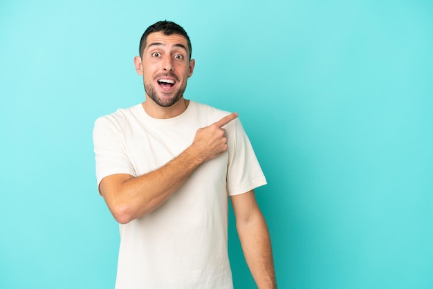 Young handsome caucasian man isolated on blue background surprised and pointing side