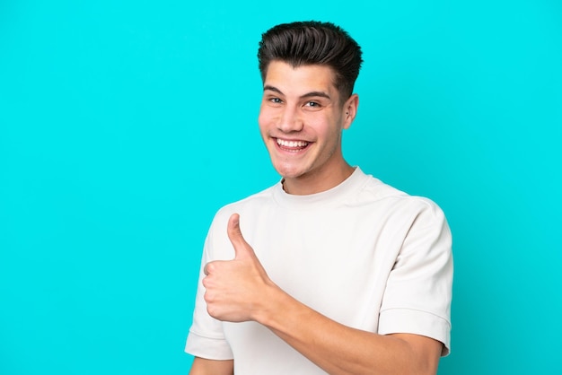 Young handsome caucasian man isolated on blue bakcground giving a thumbs up gesture