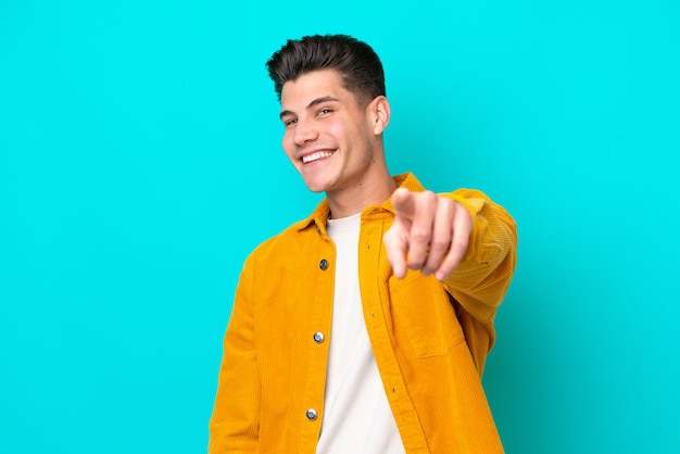 Young handsome caucasian man isolated on blue bakcground pointing front with happy expression