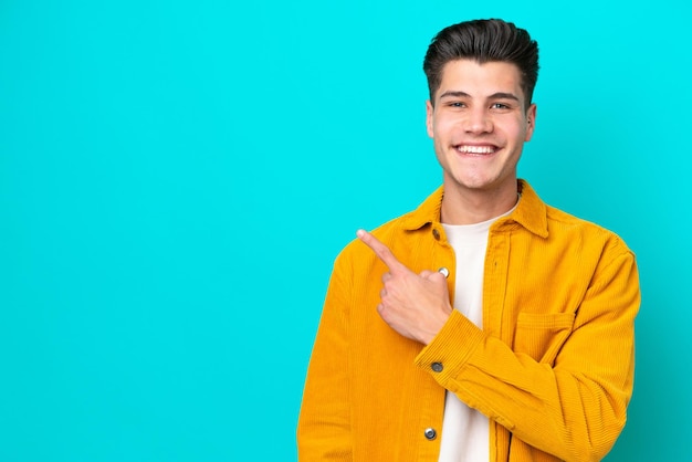 Young handsome caucasian man isolated on blue bakcground pointing to the side to present a product