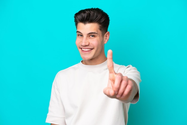 Young handsome caucasian man isolated on blue bakcground showing and lifting a finger