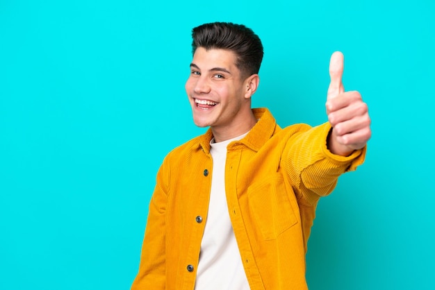 Young handsome caucasian man isolated on blue bakcground with thumbs up because something good has happened