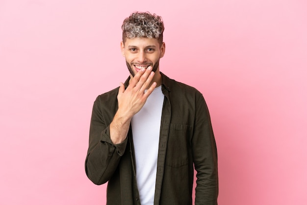 Young handsome caucasian man isolated on pink background happy and smiling covering mouth with hand