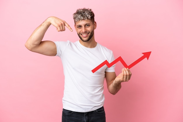 Young handsome caucasian man isolated on pink background holding a catching a rising arrow and pointing it