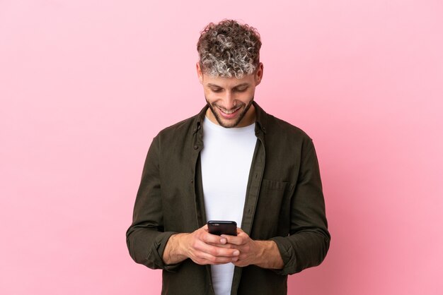 Photo young handsome caucasian man isolated on pink background sending a message with the mobile