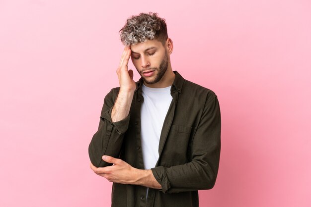 Young handsome caucasian man isolated on pink background with headache