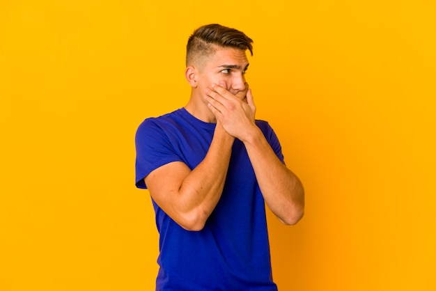 Young handsome caucasian man isolated thoughtful looking to a copy space covering mouth with hand.