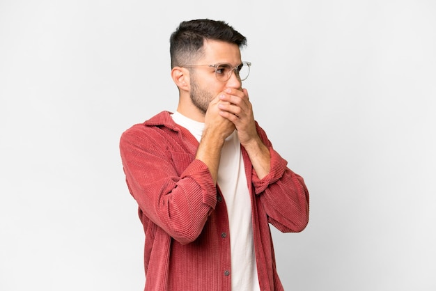 Young handsome caucasian man over isolated white background covering mouth and looking to the side