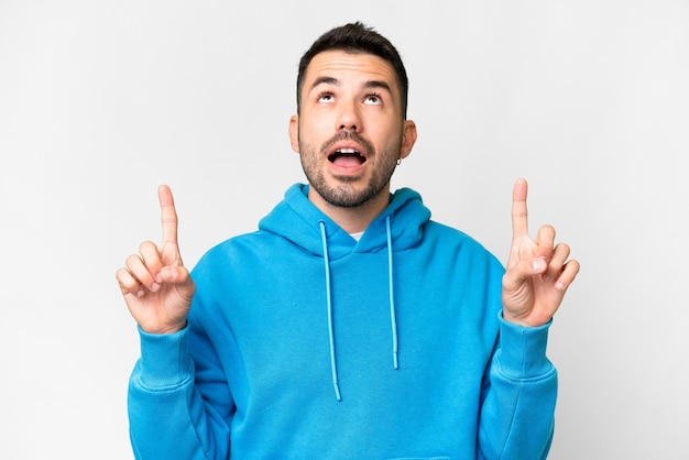 Young handsome caucasian man over isolated white background surprised and pointing up