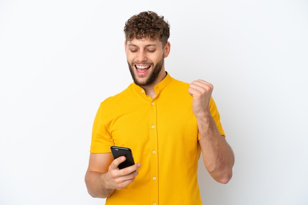 Young handsome caucasian man isolated on white background with phone in victory position