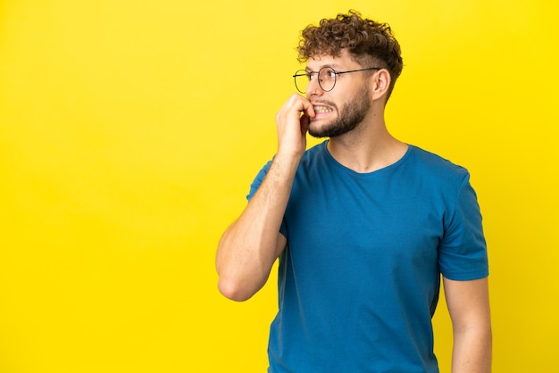 Young handsome caucasian man isolated on yellow background is a little bit nervous