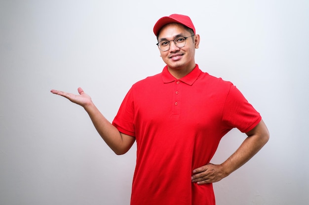 Young handsome chinese delivery man wearing cap standing over isolated white background with a big smile on face pointing with hand and finger to the side looking at the camera