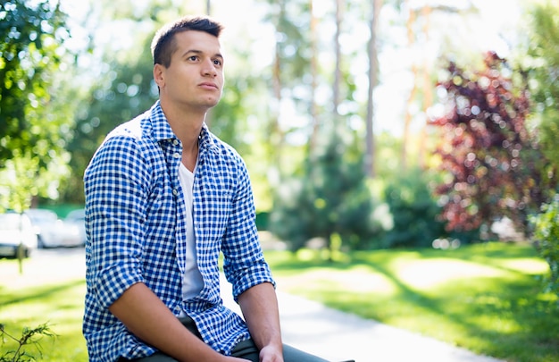 Young handsome confident man in a checkered shirt while he rests on the bench outdoors