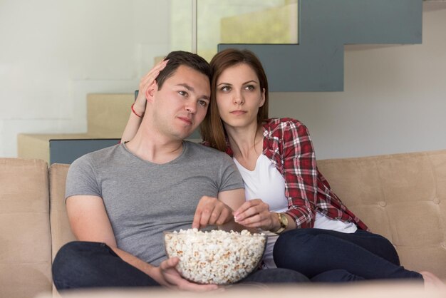 young handsome couple enjoying free time watching television with popcorn in their luxury home villa