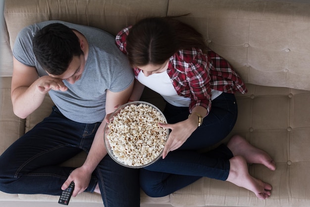 young handsome couple enjoying free time watching television with popcorn in their luxury home villa