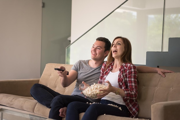 young handsome couple enjoying free time watching television with popcorn in their luxury home villa