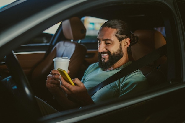 Young handsome darkhaired man holding a phone and driving a car