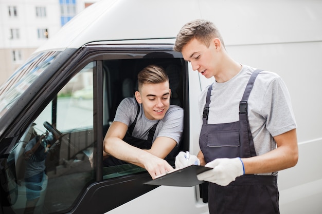 A young handsome guy wearing uniform is pointing at the clipboard. Another worker wearing uniform is looking at the clipboard. House move, mover service.