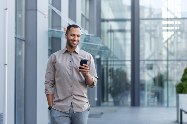 A young handsome hispanic africanamerican man walks down the street near an office center he is