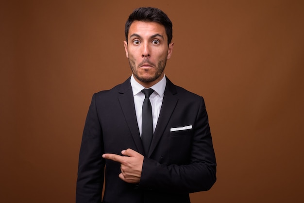 Young handsome Hispanic businessman against brown background