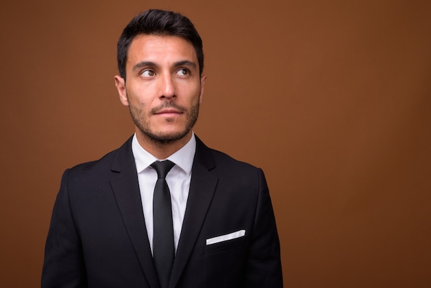 Young handsome Hispanic businessman against brown background