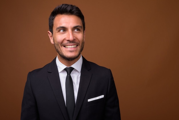 Young handsome Hispanic businessman against brown background