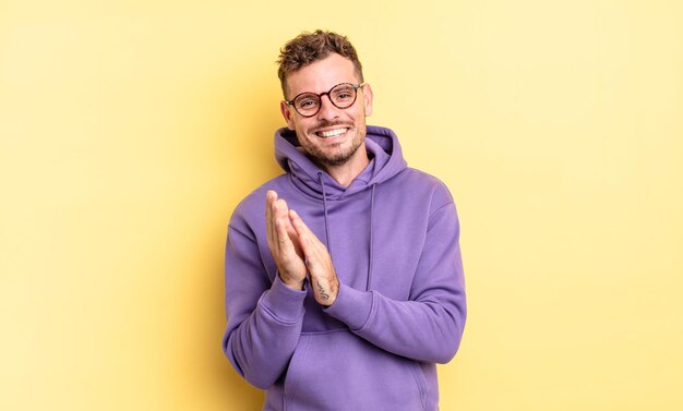 Photo young handsome hispanic man feeling happy and successful, smiling and clapping hands, saying congratulations with an applause