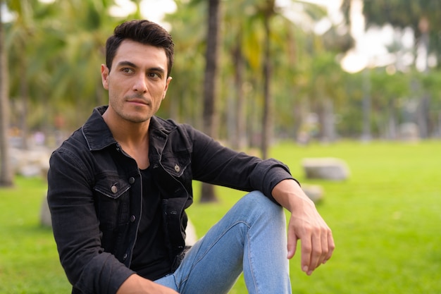 Young handsome Hispanic man sitting and thinking at the park